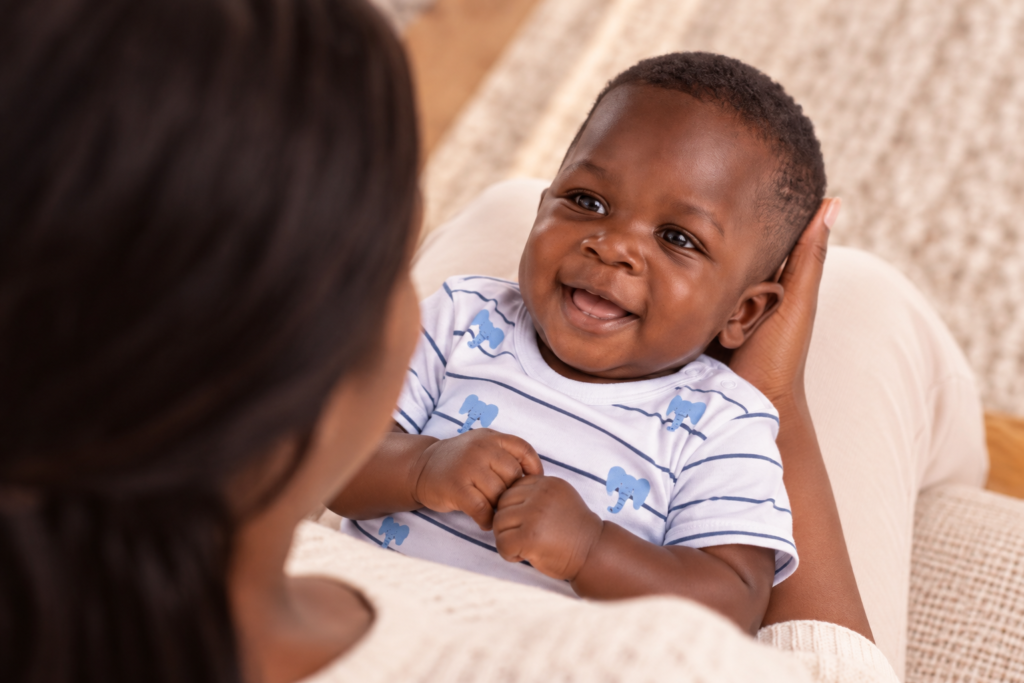 a imagem mostra um bebê sorrindo para a mãe e vestindo um macacão infantil da alphabeto brancom com estampas de elefantes. A imagem ilustra uma matéria sobre saltos de desenvolvimento.